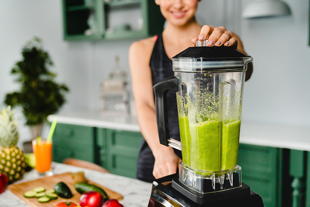 person blending a green smoothie in a kitchen